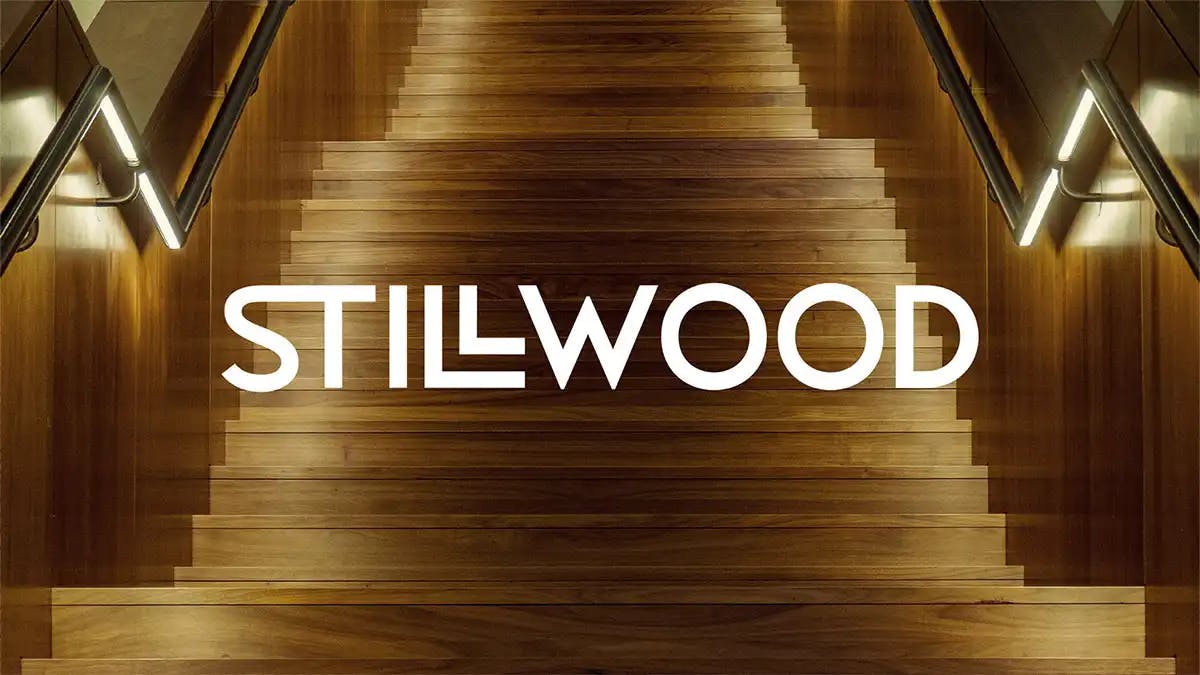 Obraz przedstawia logo Stillwood na tle eleganckich drewnianych schodów